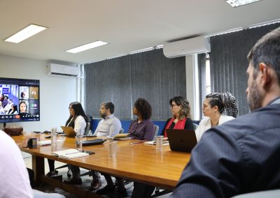 Participantes acompanham reunião presencial do Projeto Olimpíadas Científicas com a SEDF, com videoconferência exibida em tela.